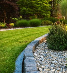 A lush green lawn with a stone border and gravel in a garden.