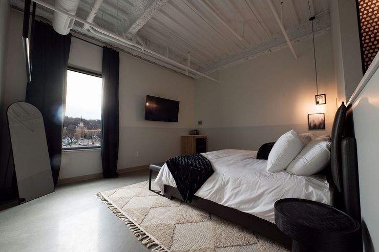 Modern bedroom with a large bed, wall-mounted TV, tall windows, and minimalist decor