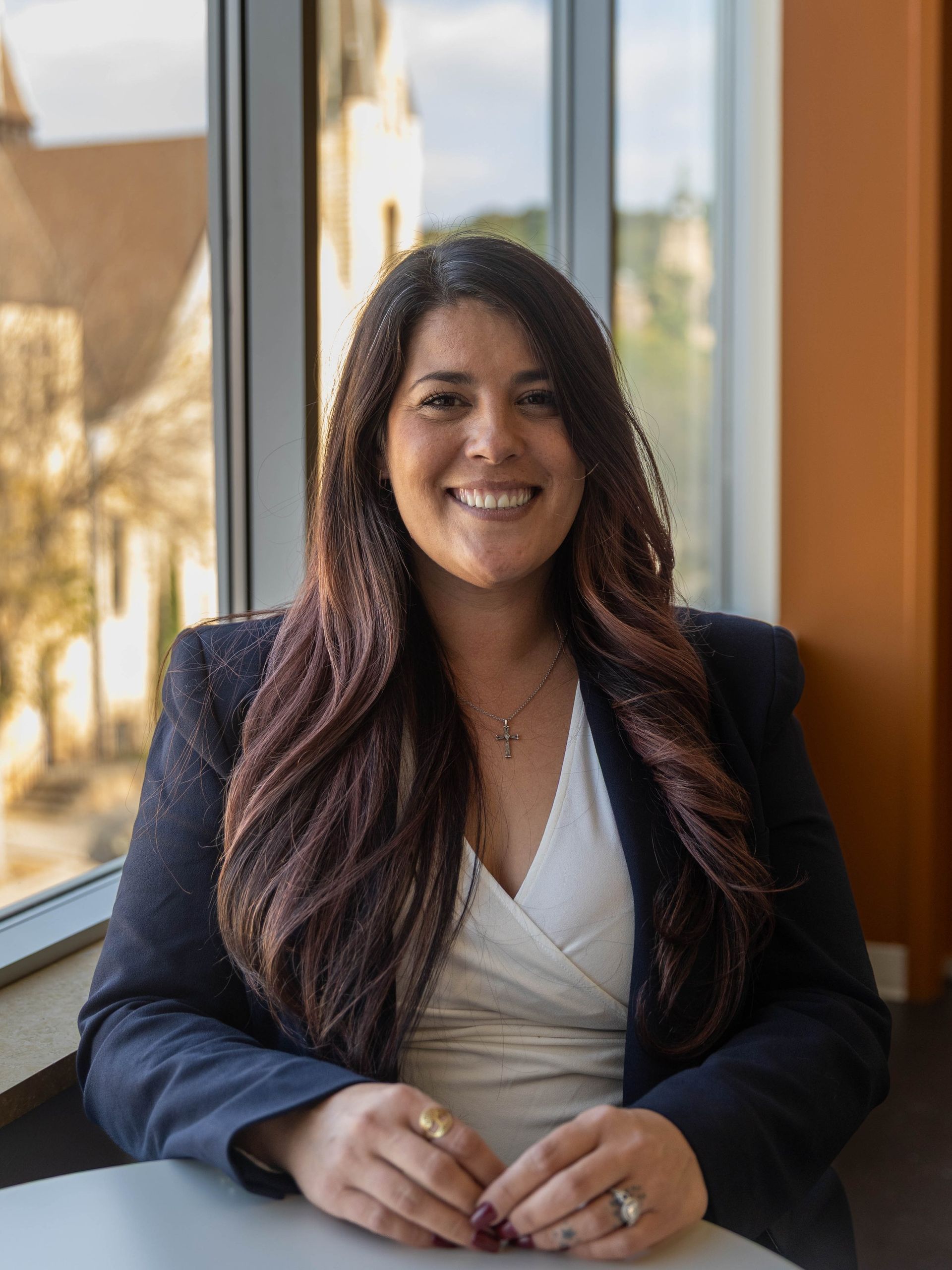 Smiling woman in a navy blazer seated by a window in a bright office.