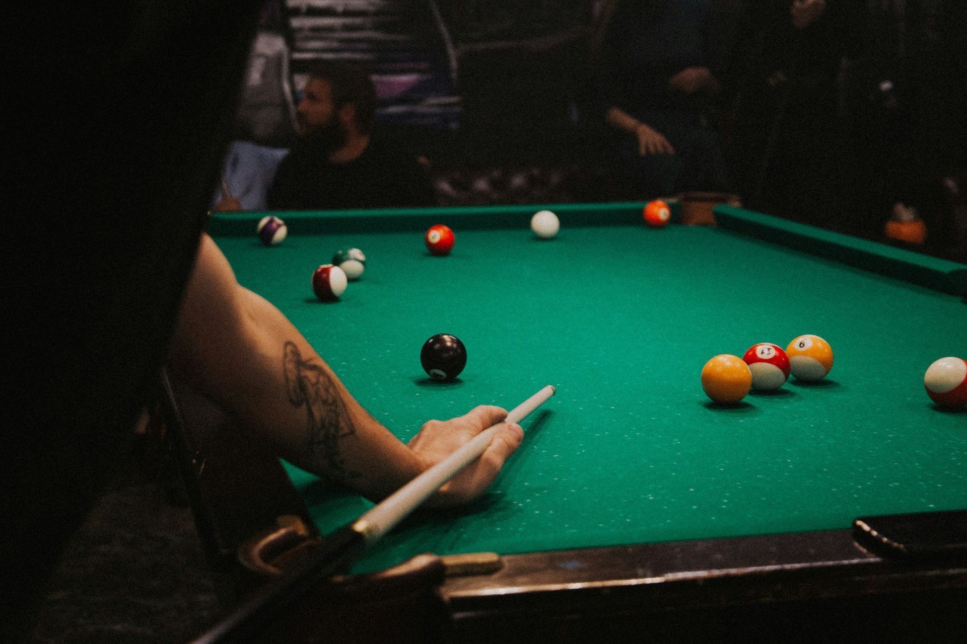 Person lining up a pool shot at a green billiards table with scattered balls.