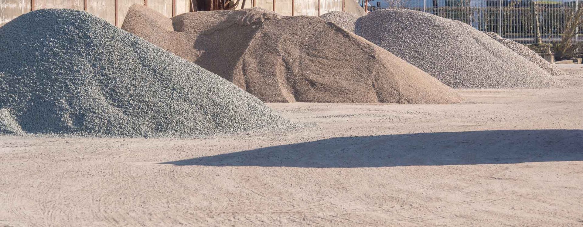 Piles of gravel and sand at a construction or quarry site under bright sunlight