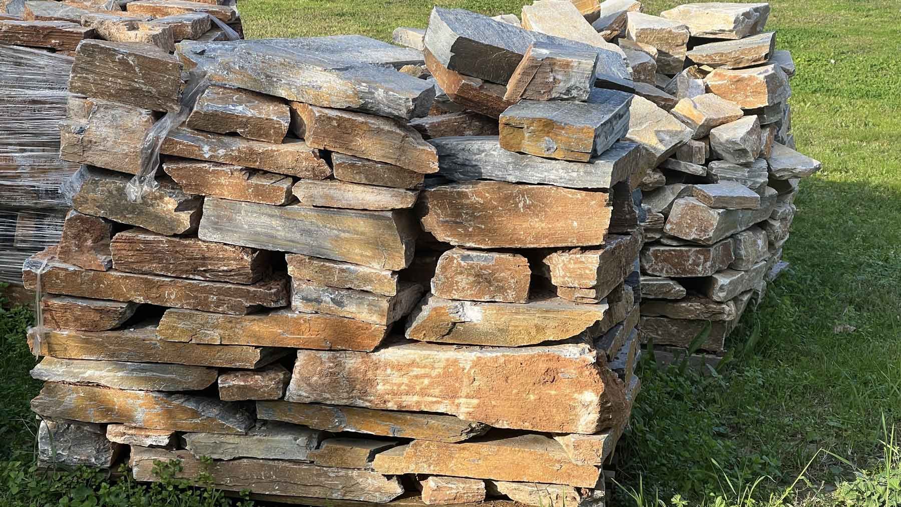 Stacked rough-cut stone slabs outdoors on grass in sunlight Stacked rough-cut stone slabs outdoors on grass in sunlight