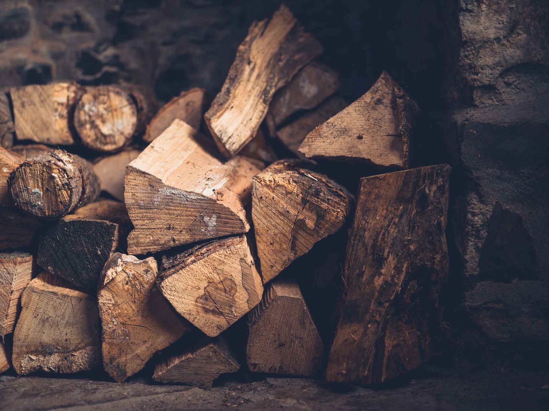 Stacked split firewood logs in a dimly lit hearth or woodpile.