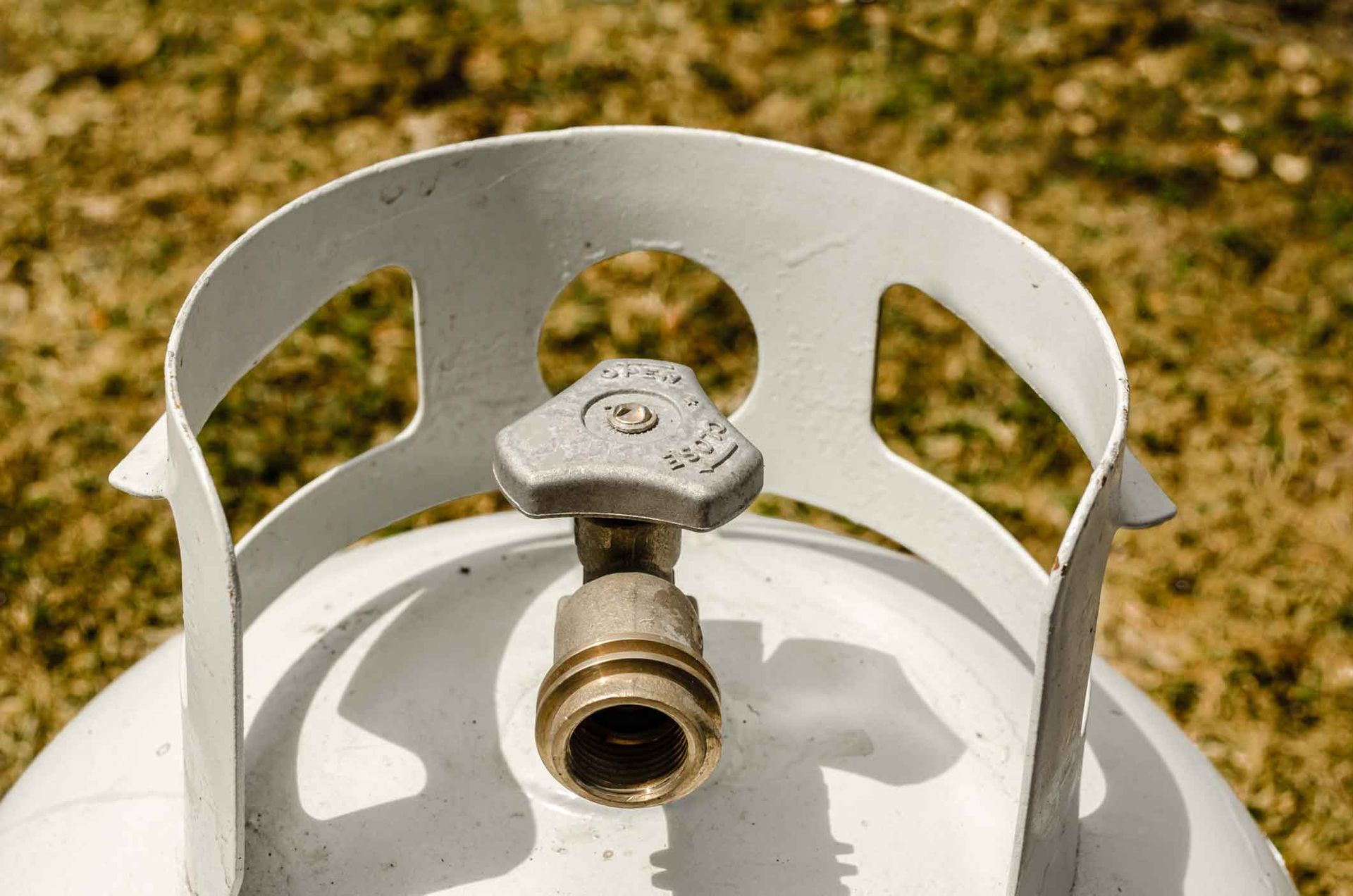 Close-up of a white propane tank valve with a brass connector outdoors on grass.