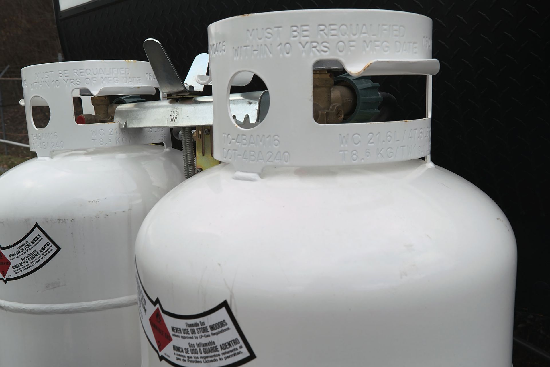 Two white propane tanks with metal handles and black valves, stacked closely together outdoors