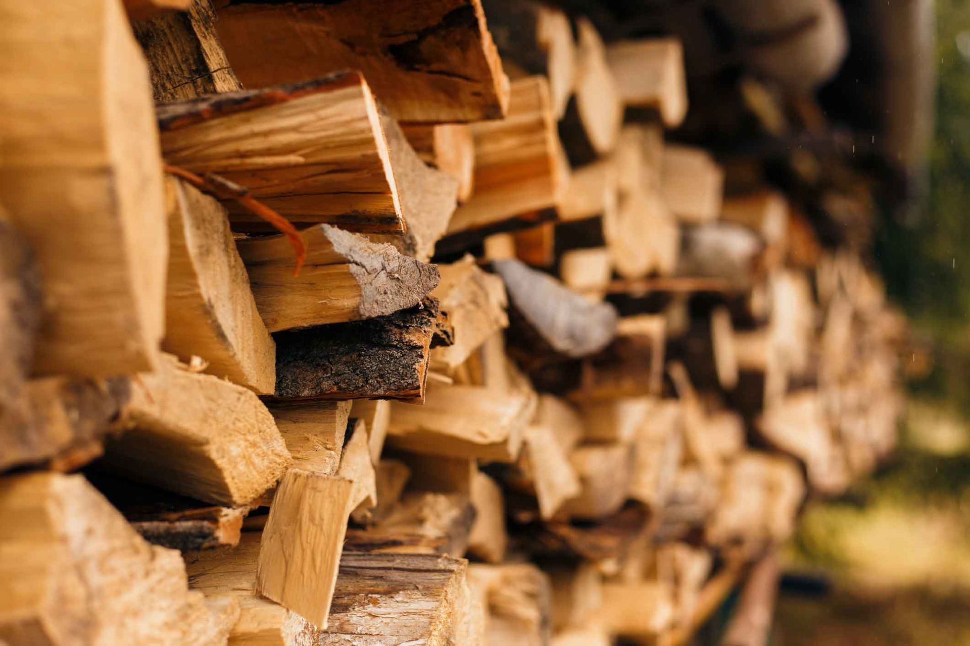 Stacked split firewood logs in warm brown tones, filling the frame in a rustic setting