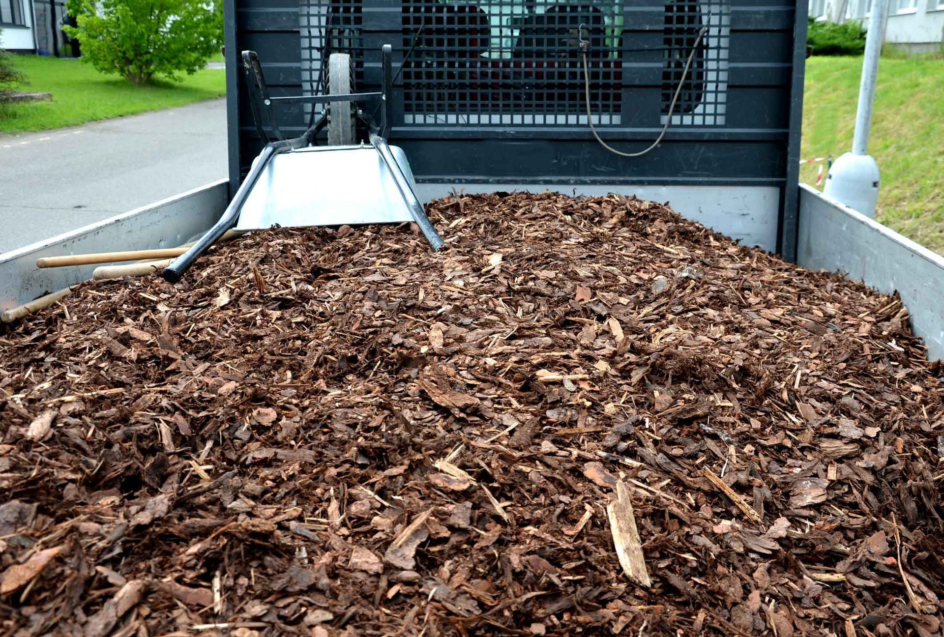 Dump trailer filled with brown mulch beside a driveway and green lawn