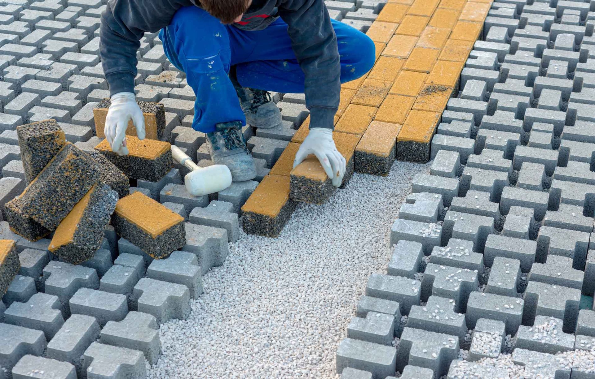 Worker laying gray and orange paving stones on a sidewalk under construction Worker laying gray and orange paving stones on a sidewalk under construction