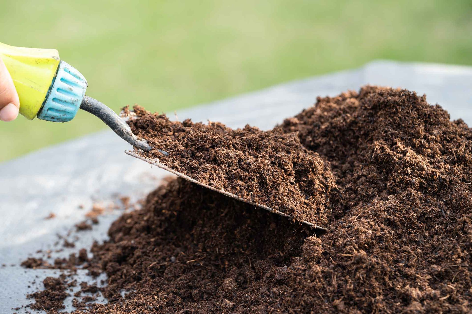 Hand trowel lifting dark soil compost from a pile outdoors