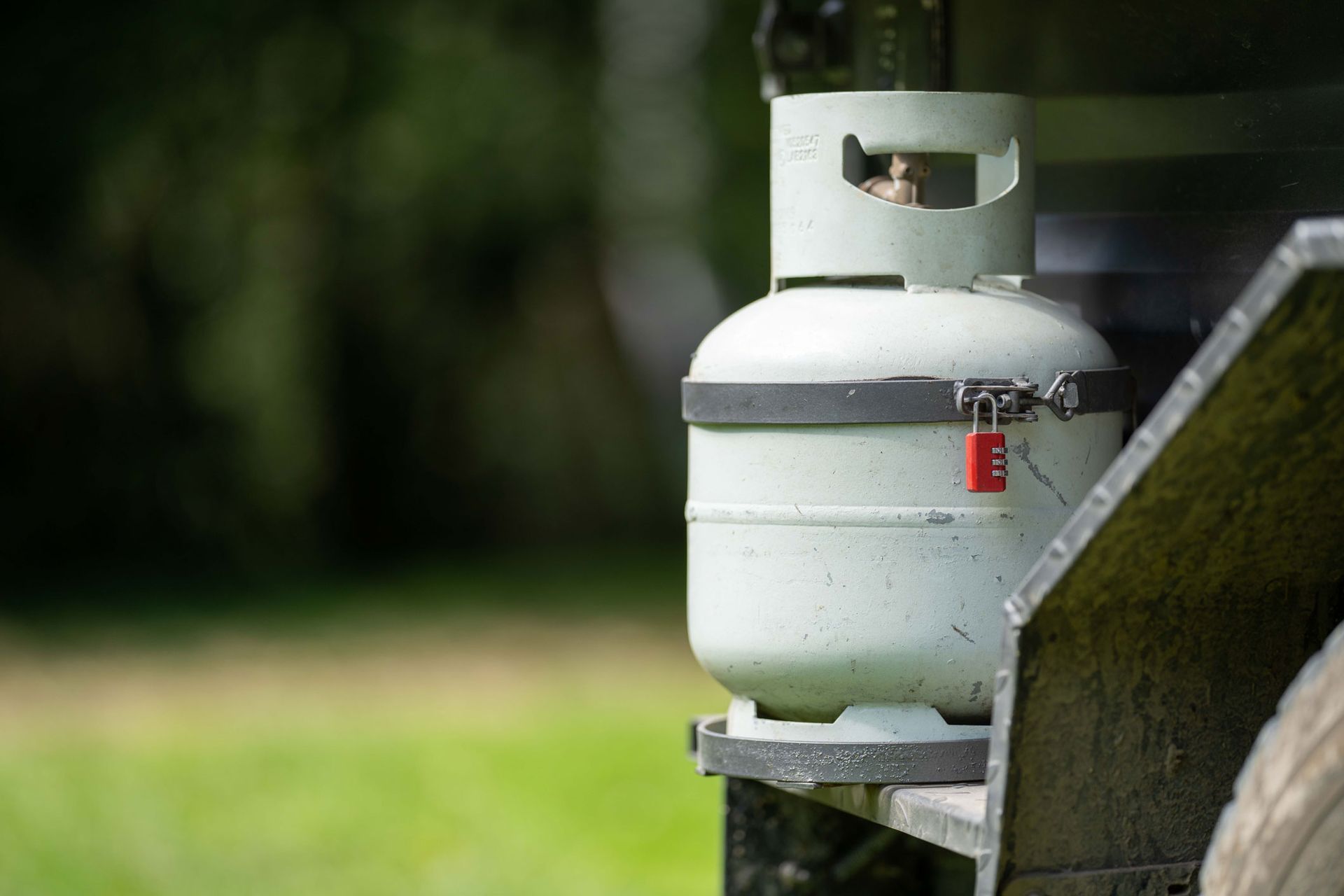 Small white propane tank mounted on a metal trailer, outdoors with a blurred green background.