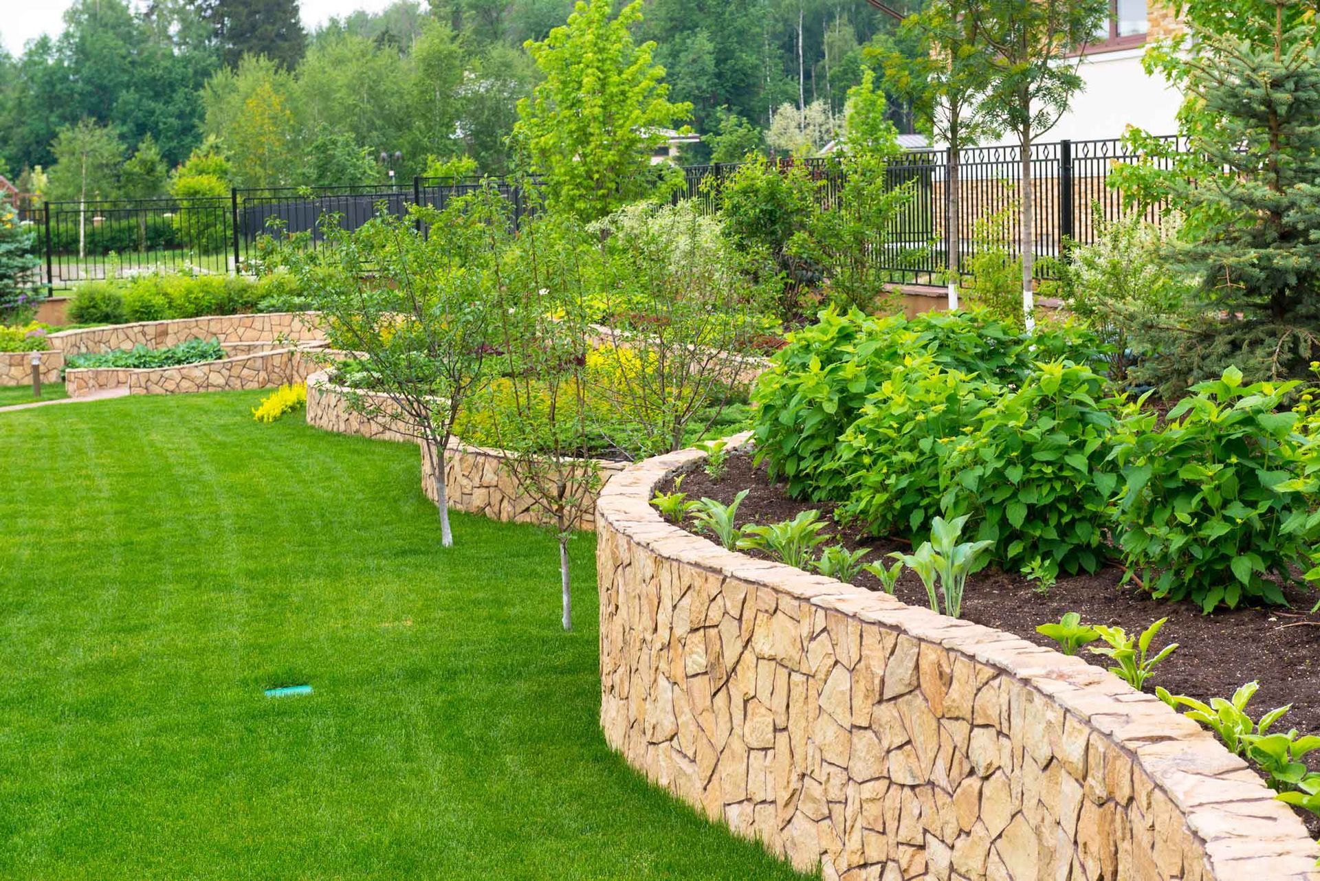 Curved stone retaining wall bordering a lush green landscaped garden with shrubs and trees Curved stone retaining wall bordering a lush green landscaped garden with shrubs and trees