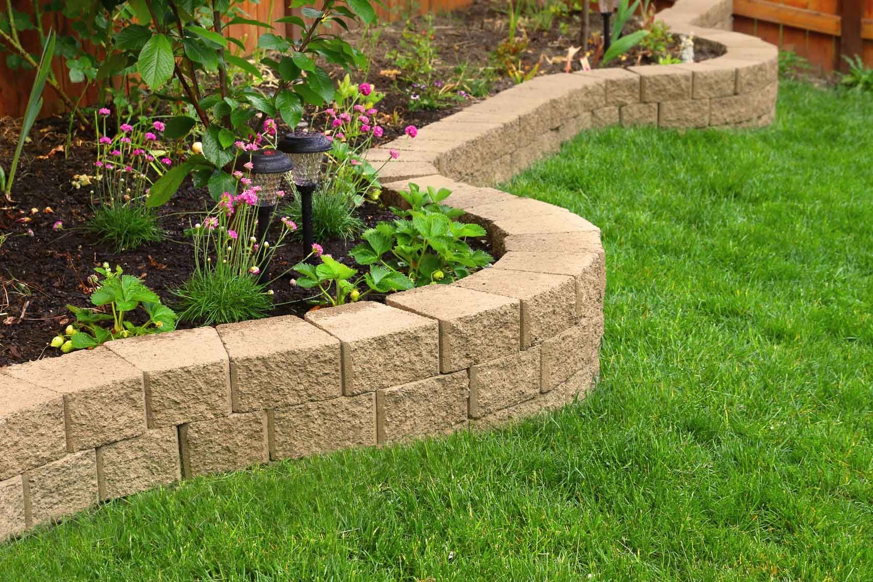 Curved tan stone garden border around a flower bed beside a green lawn