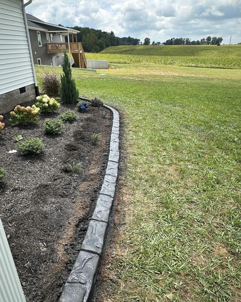 A concrete curb is being installed in a yard next to a house.