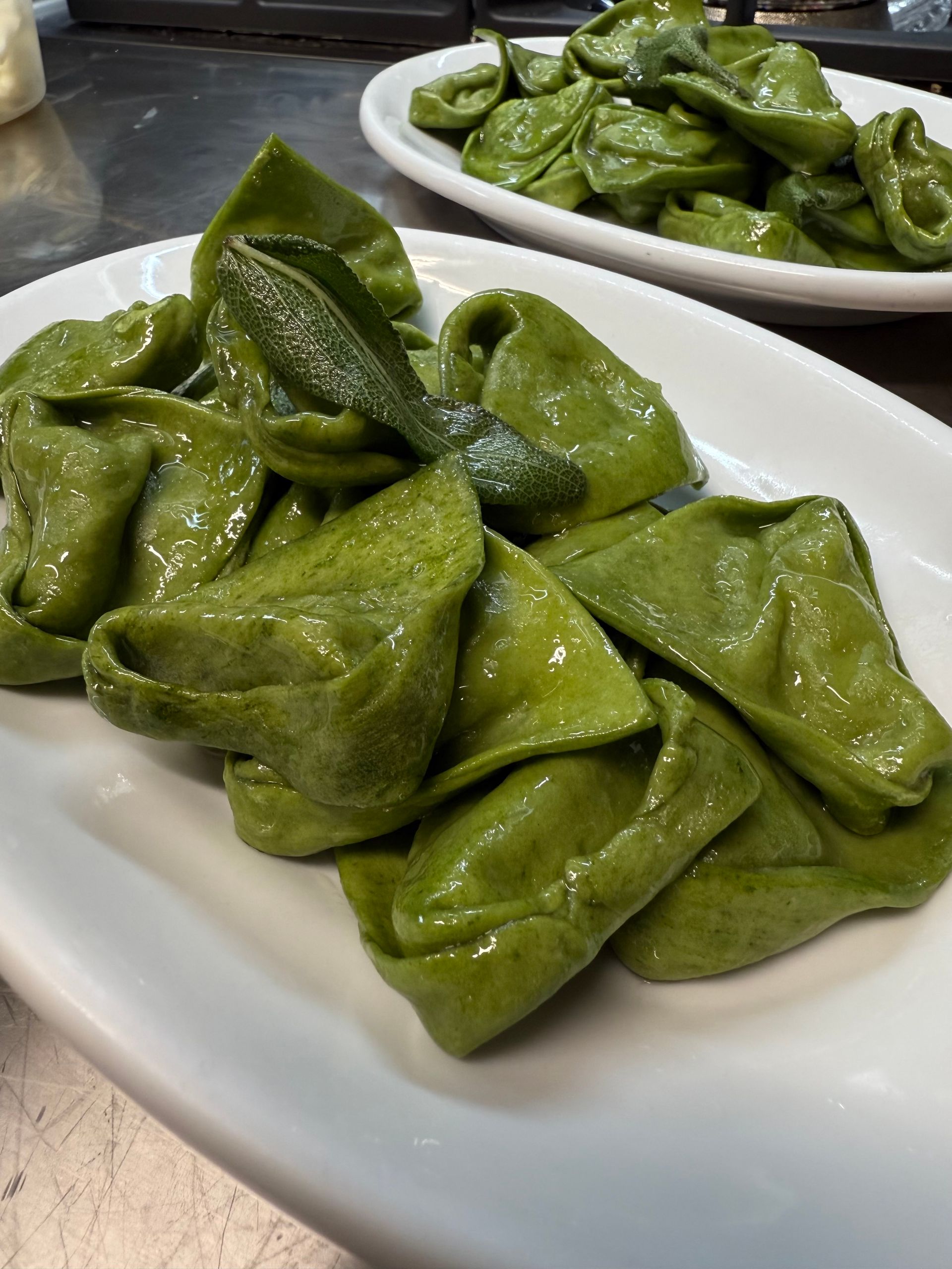Pasta verde su un piatto bianco, un altro piatto di pasta sullo sfondo.