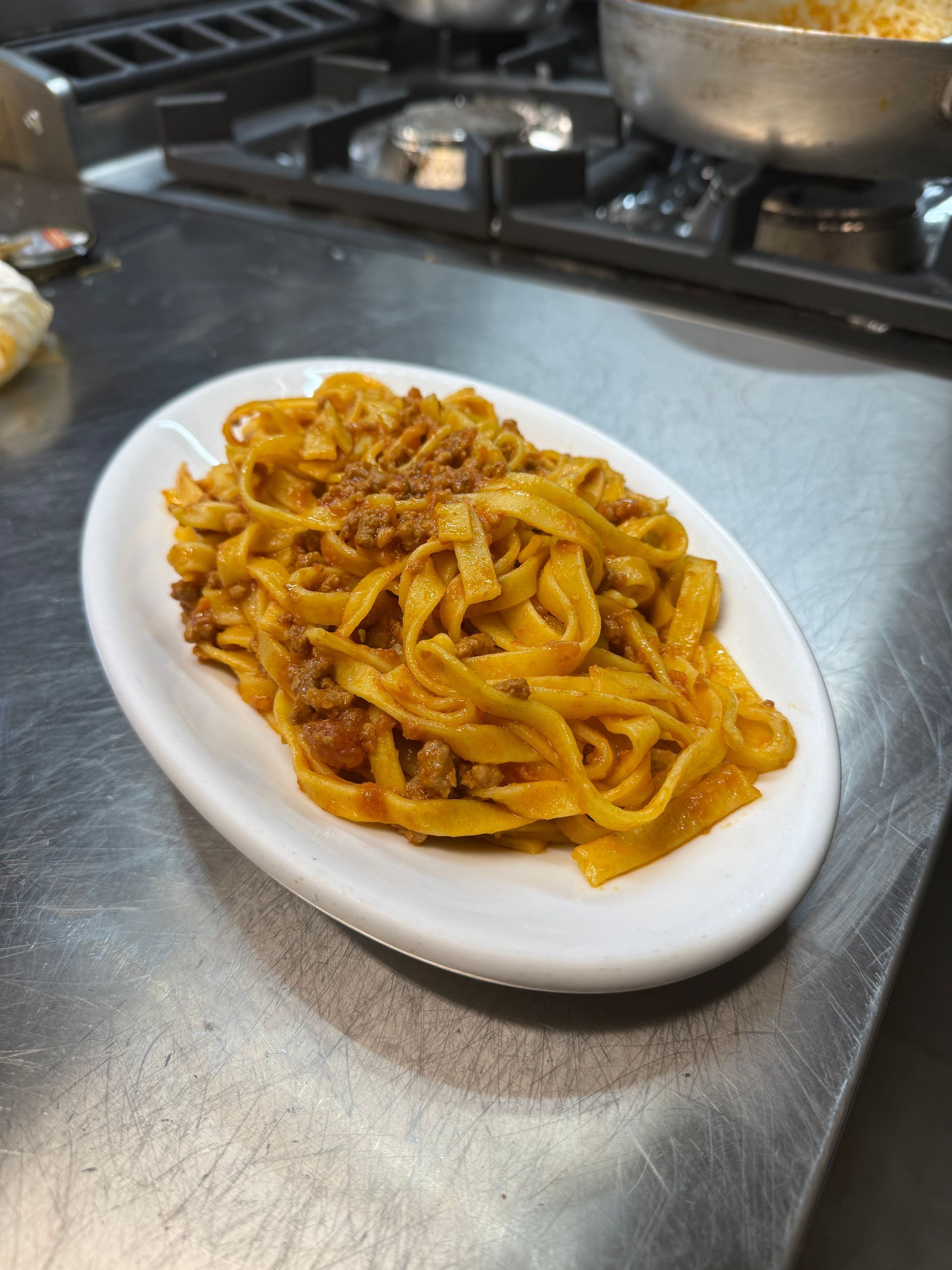 Piatto di tagliatelle al ragĂą su una superficie in acciaio inox vicino ai fornelli.
