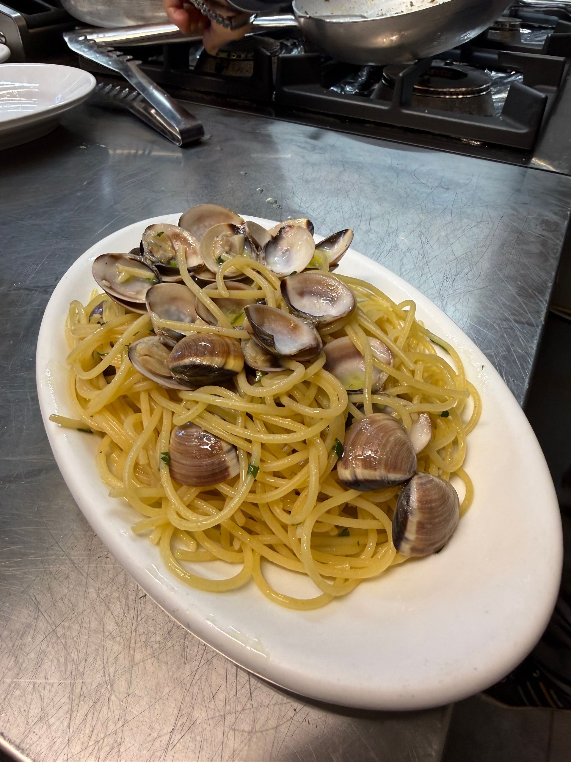 Spaghetti alle vongole in un piatto ovale bianco su un piano di lavoro in acciaio inox.