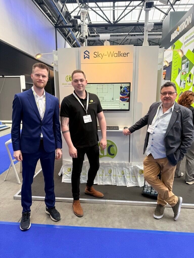 Three men posing in front of a trade show booth with a screen and display stand