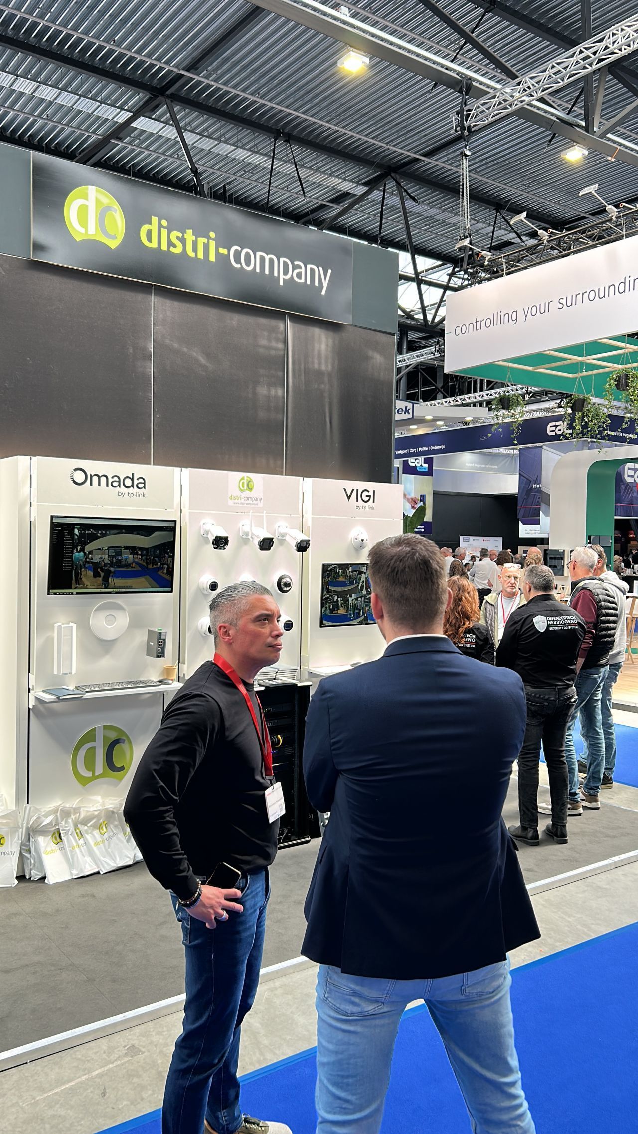 Two men talking at a trade show booth under a black and green “distri…” banner.