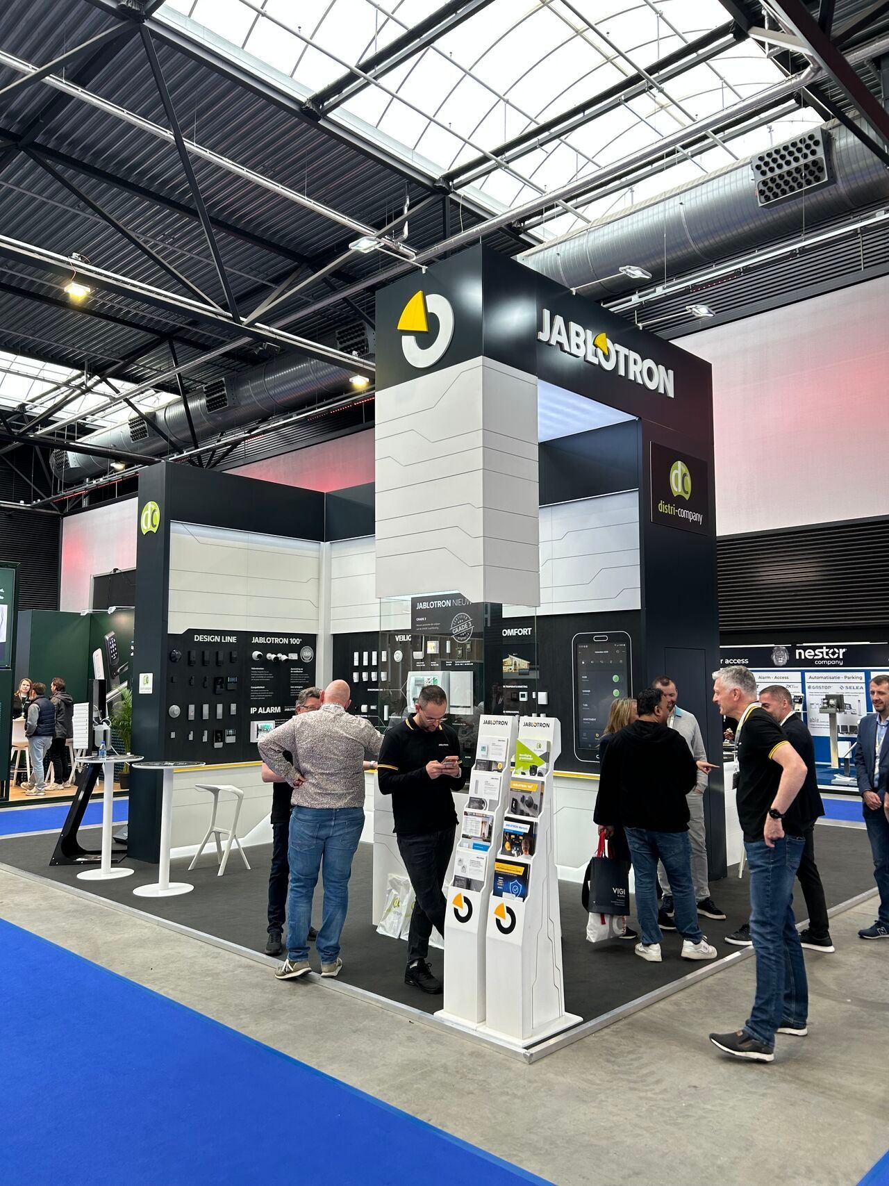 Trade show booth with people gathered around a display under a high industrial ceiling