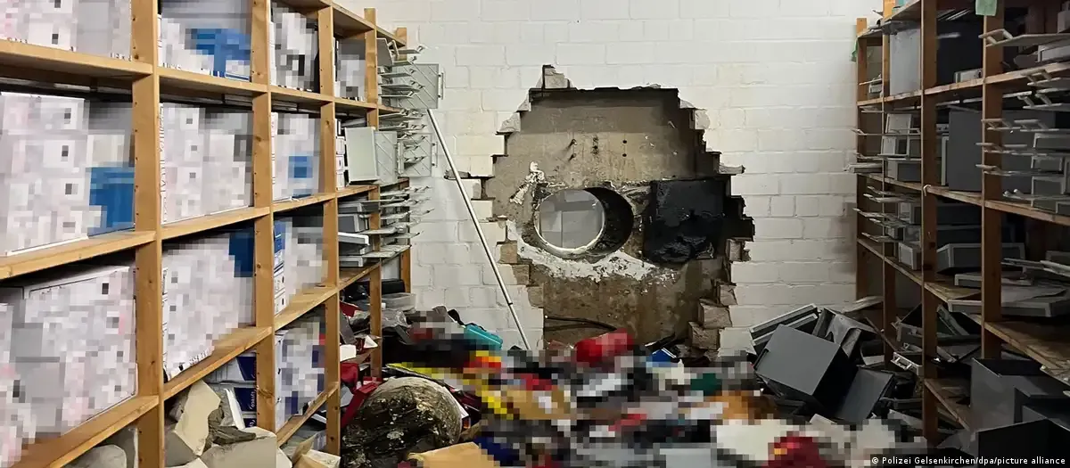 A storage room with shelves filled with boxes, showing a large hole broken through a cinder block back wall. Company Without Sky-Walker