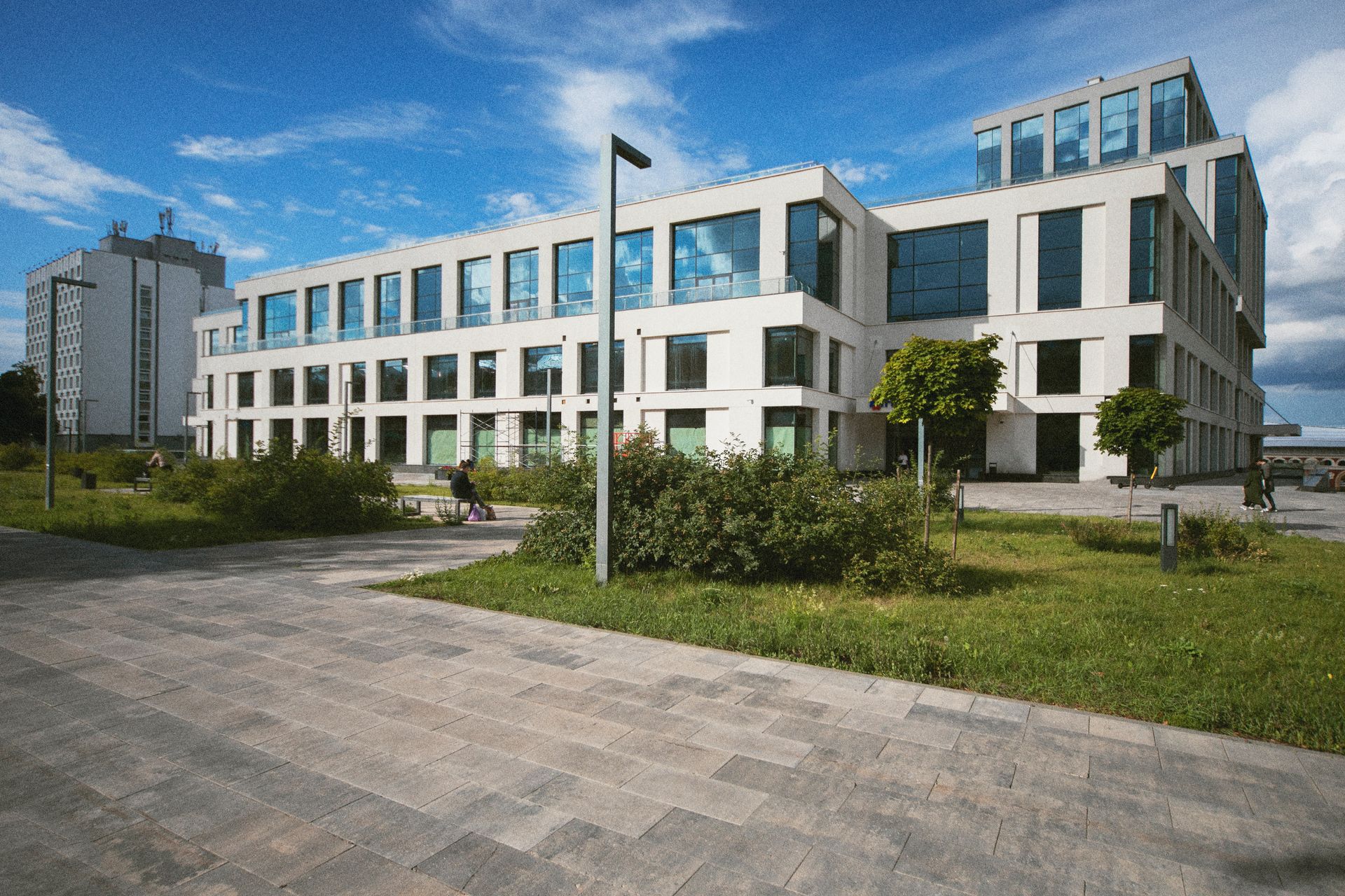 A modern, multi-story office building with a white facade and large windows, set by a green lawn and paved walkway.