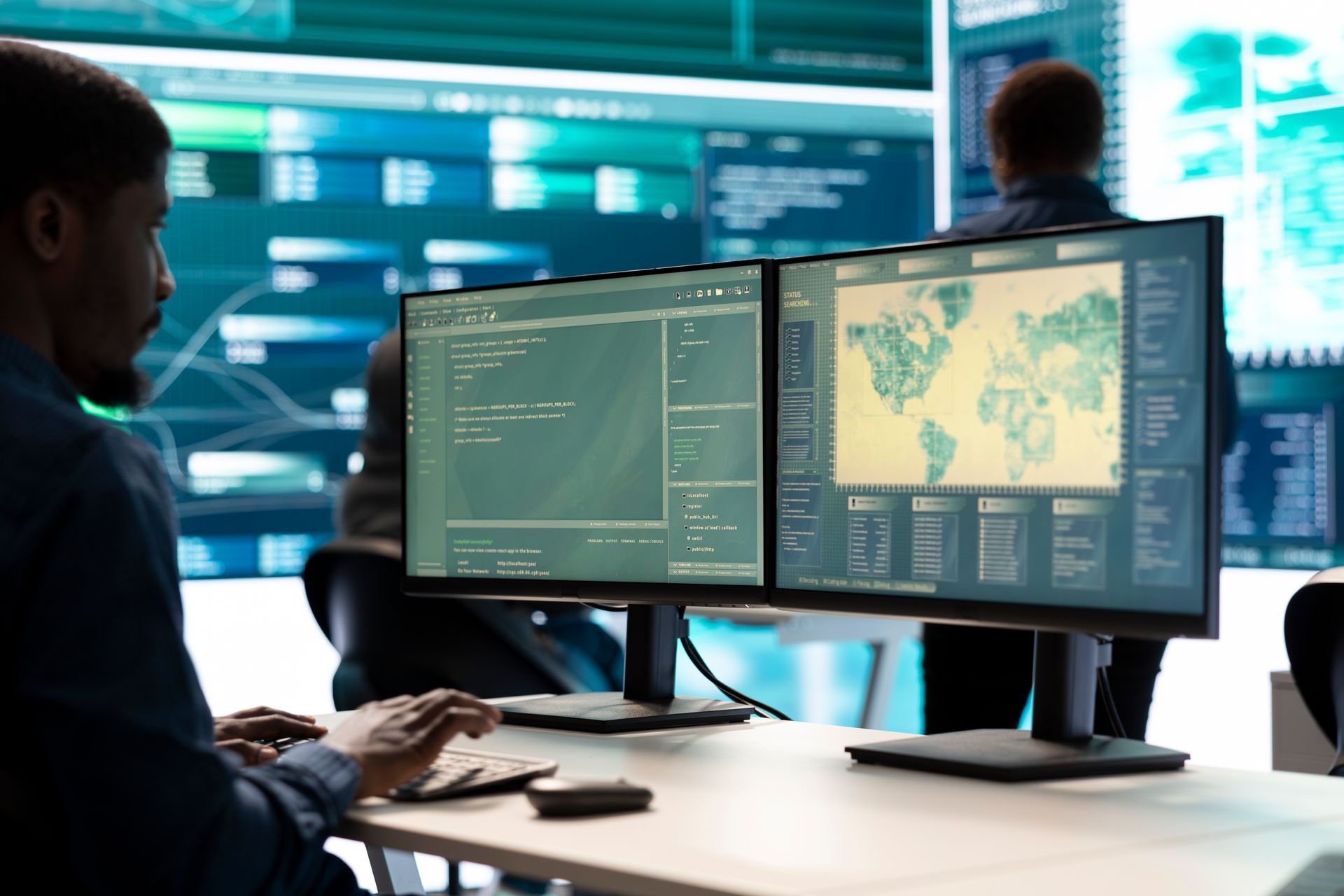 Operator working in a control room with dual monitors displaying real-time GIS data.