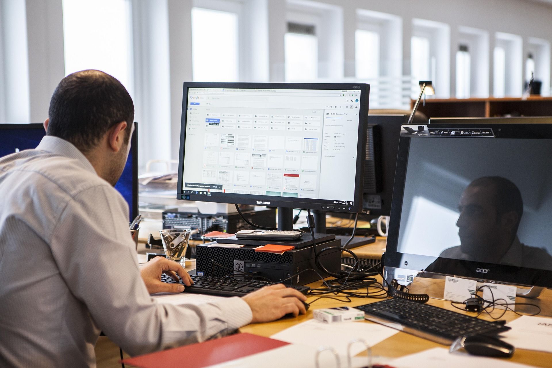A person working at a desk with multiple computer screens in an office setting. looking over data A person working at a desk with multiple computer screens in an office setting. looking over data