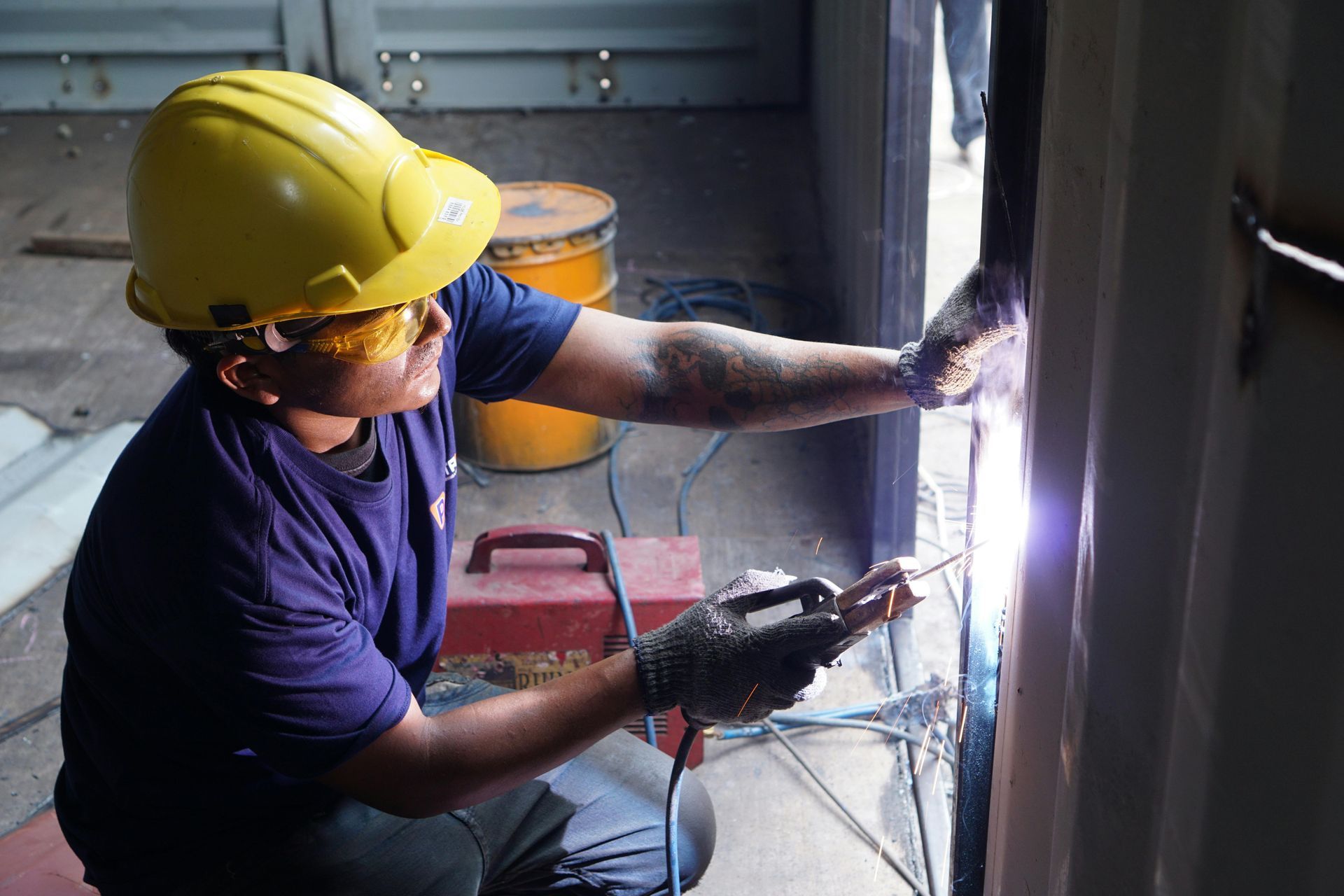 Welder in yellow hard hat and protective eyewear, welding metal on a structure.