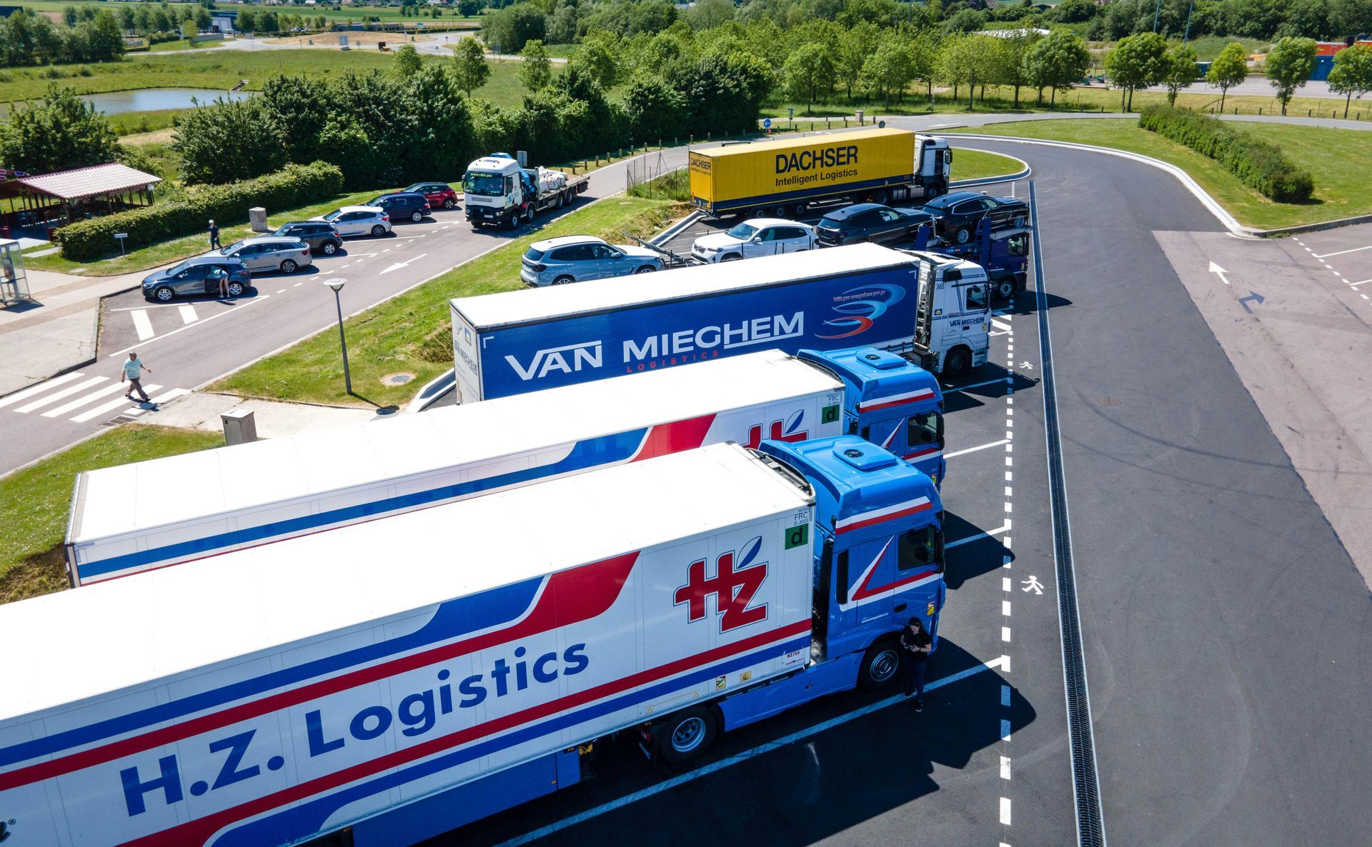 Trucks parked at a rest stop; H.Z. Logistics, Van Midden, and other transport trucks. Green trees in the background.