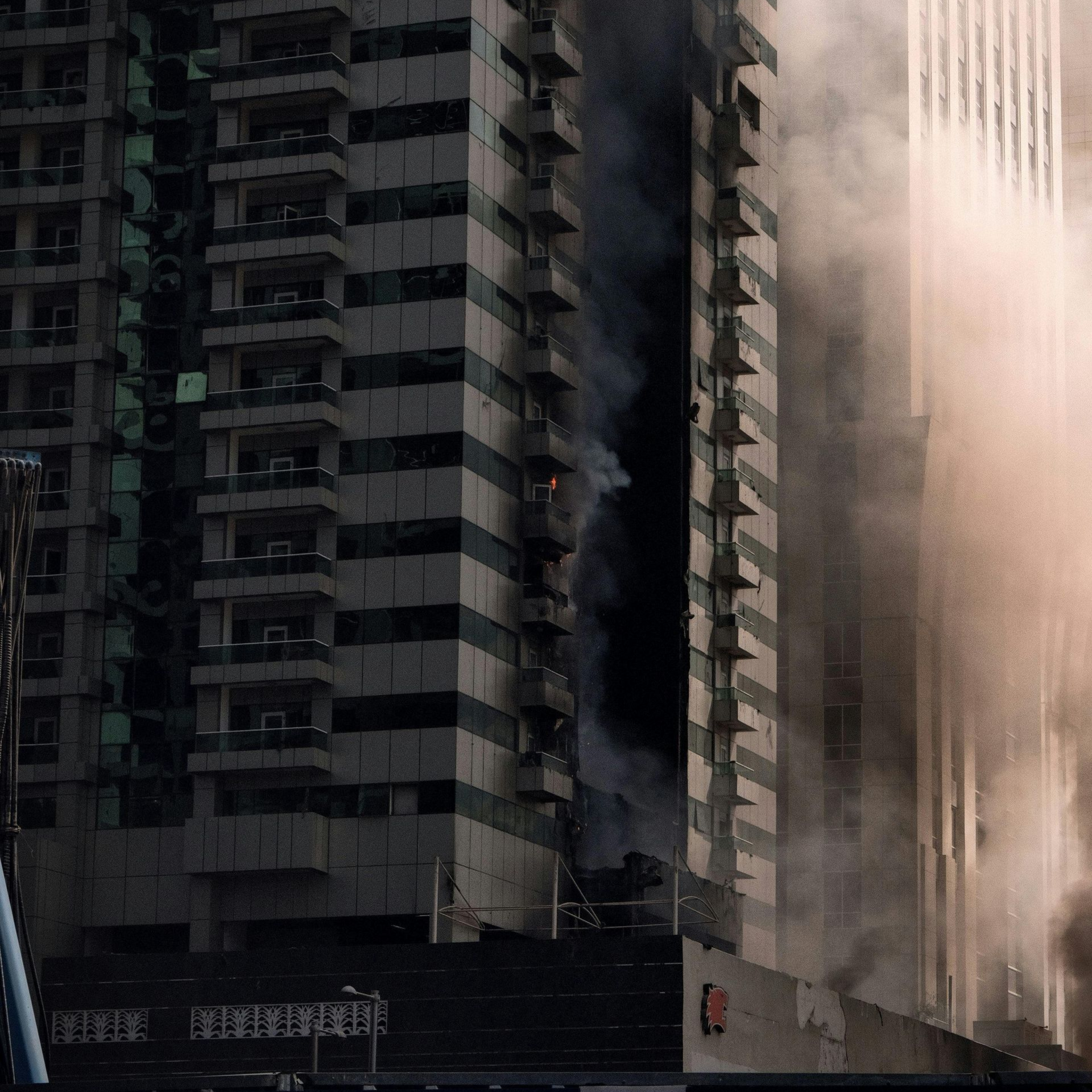 Tall apartment buildings shrouded in dust and smoke, with a dark street-level barrier in front