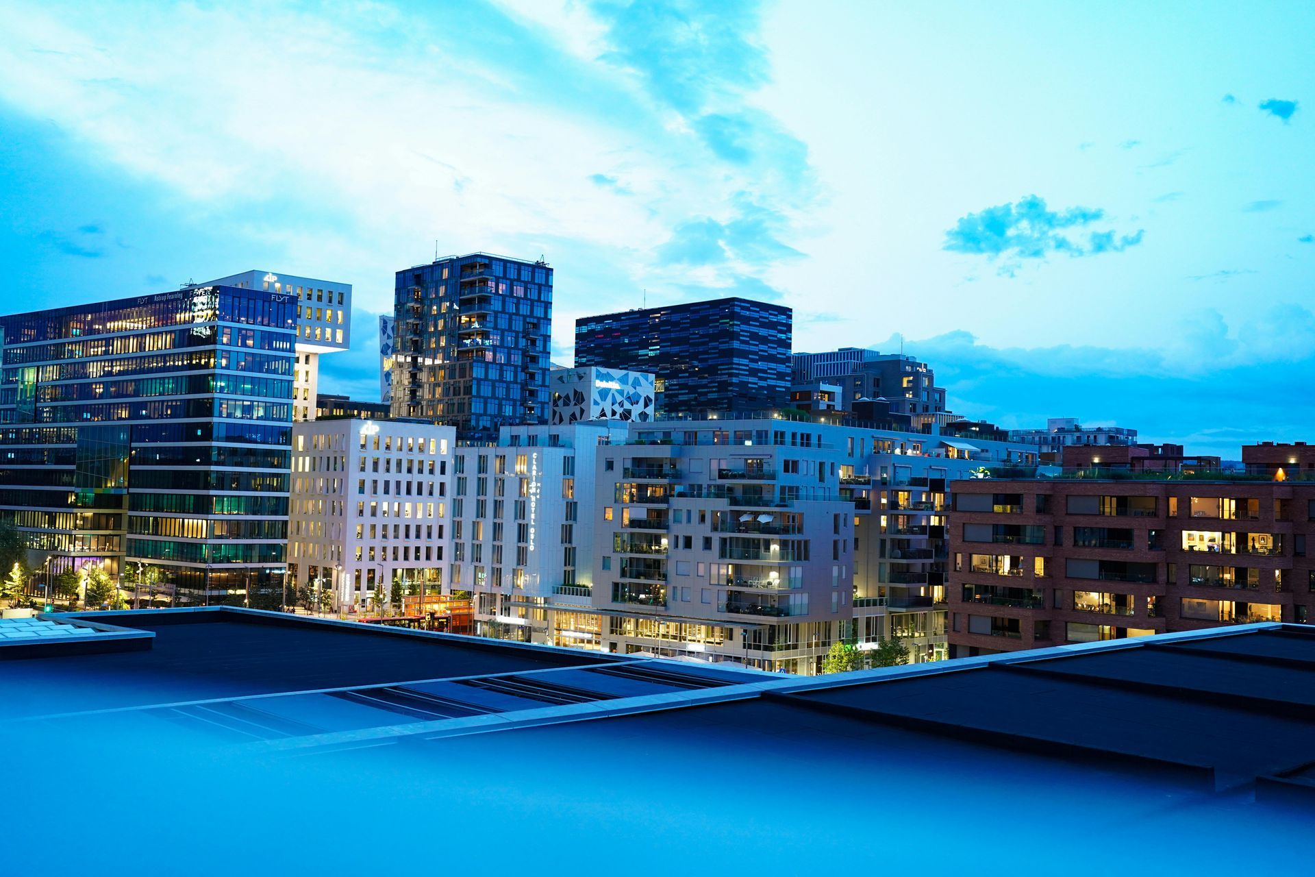 City skyline at dusk with illuminated modern buildings reflected in blue water