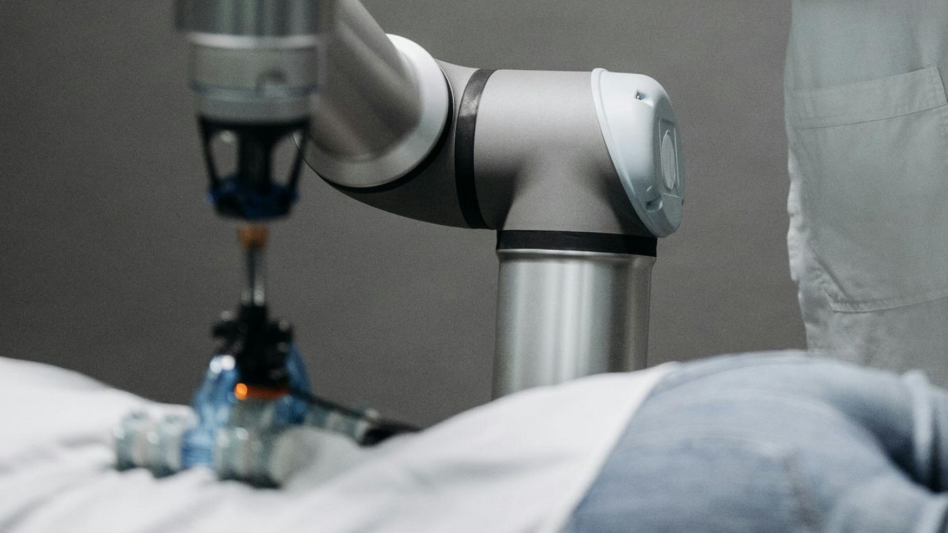 Doctor oversees robot arm drilling on patient lying on examination table.
