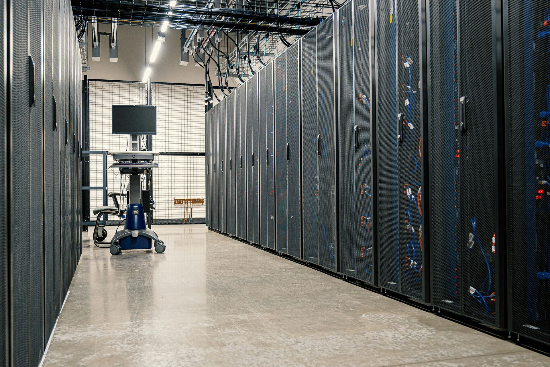 Rows of black server racks in a bright data center with a mobile monitor stand in the foreground.