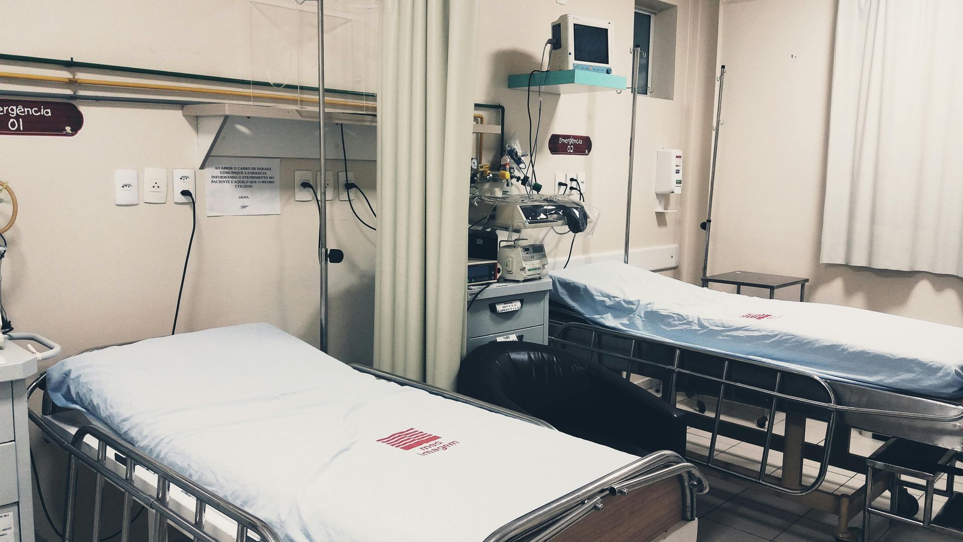 A hospital room featuring two patient beds with white linens, medical equipment, and a curtain partition.