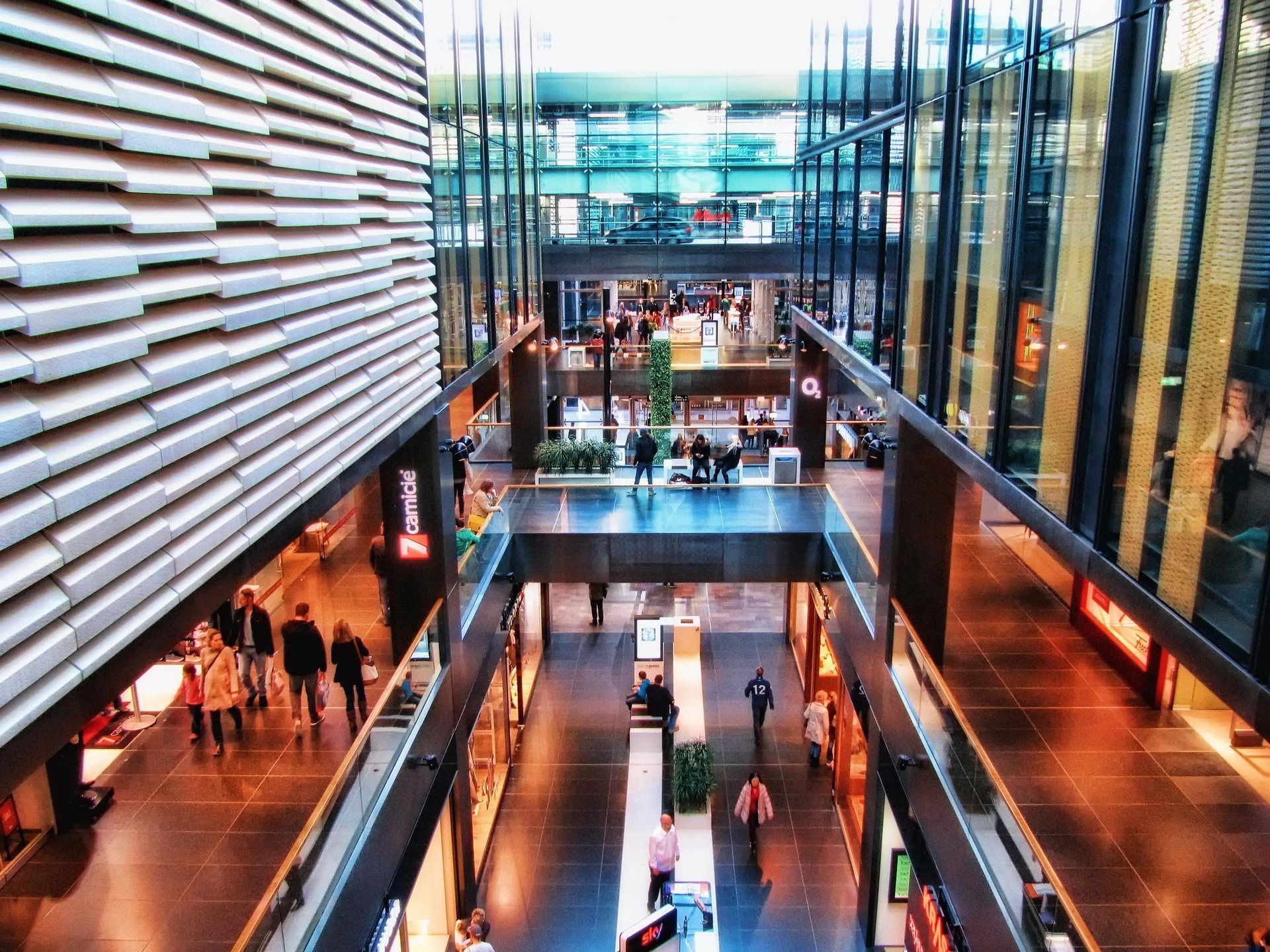 A multi-level shopping center interior with modern architecture, glass railings, and people walking on polished floors. Building management Sky-Walker