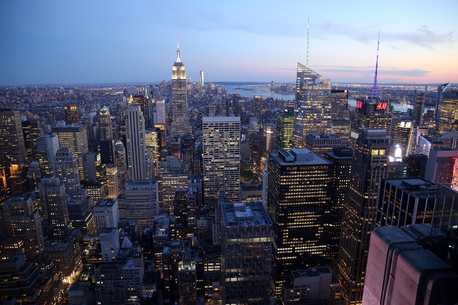 Aerial view of the New York City skyline at dusk, featuring the Empire State Building illuminated against a blue sky.