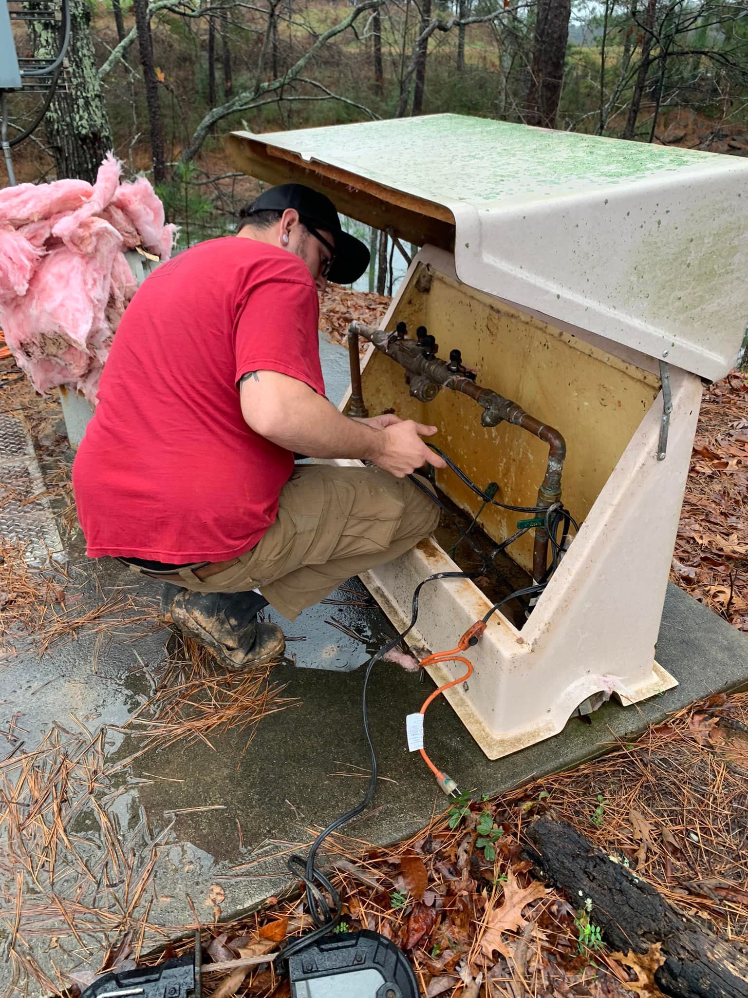 A man in a red shirt is working on a machine outside.