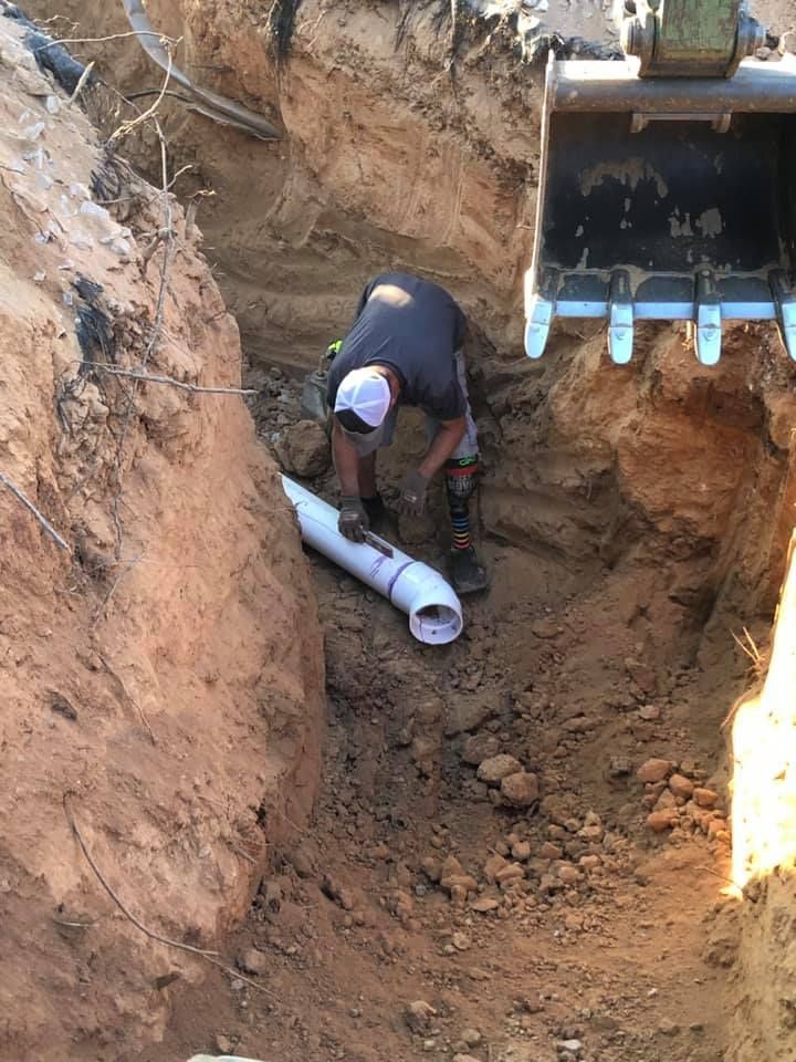 A man is working on a pipe in the dirt.