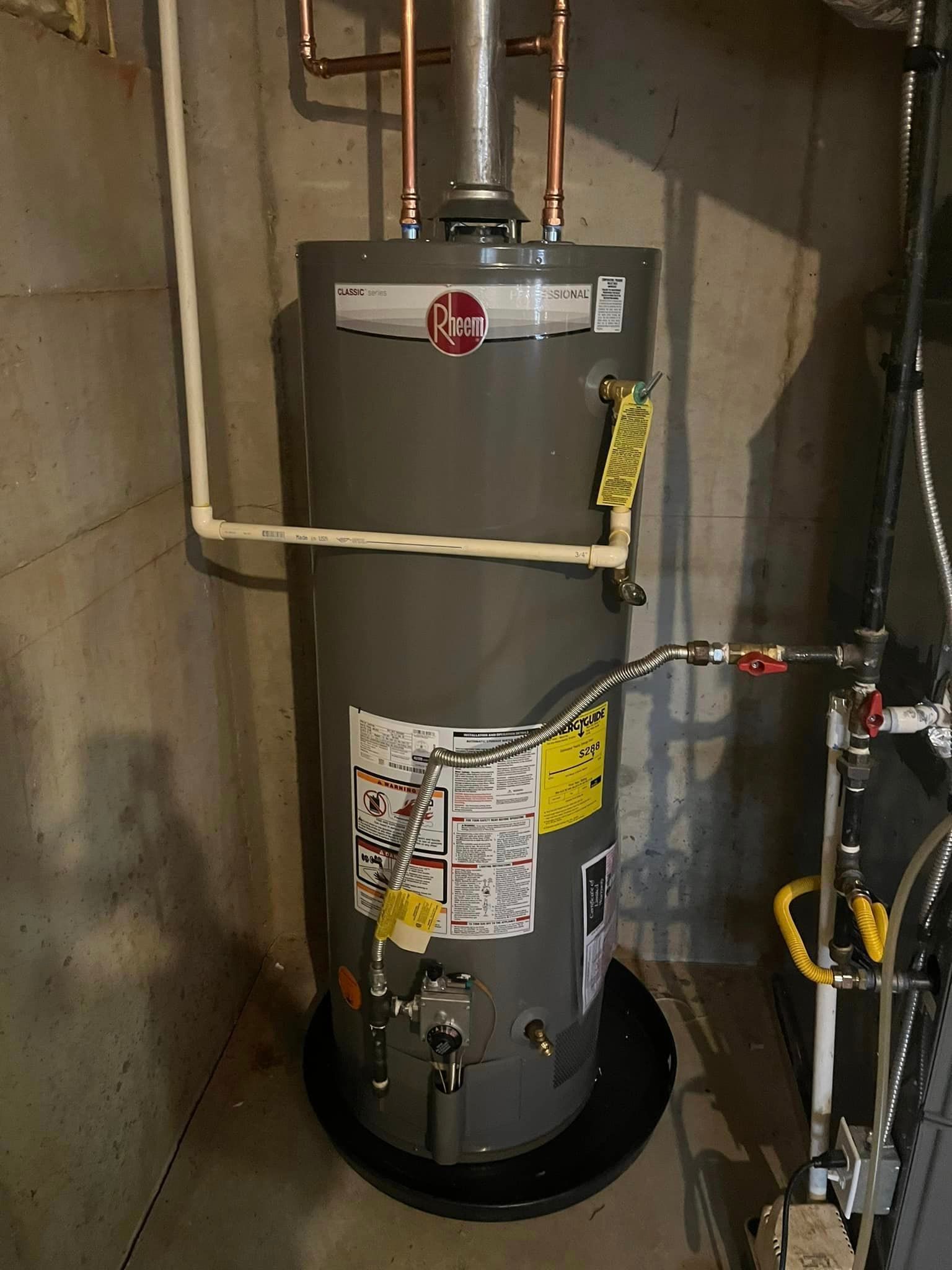 A water heater is sitting in a basement next to a pipe.