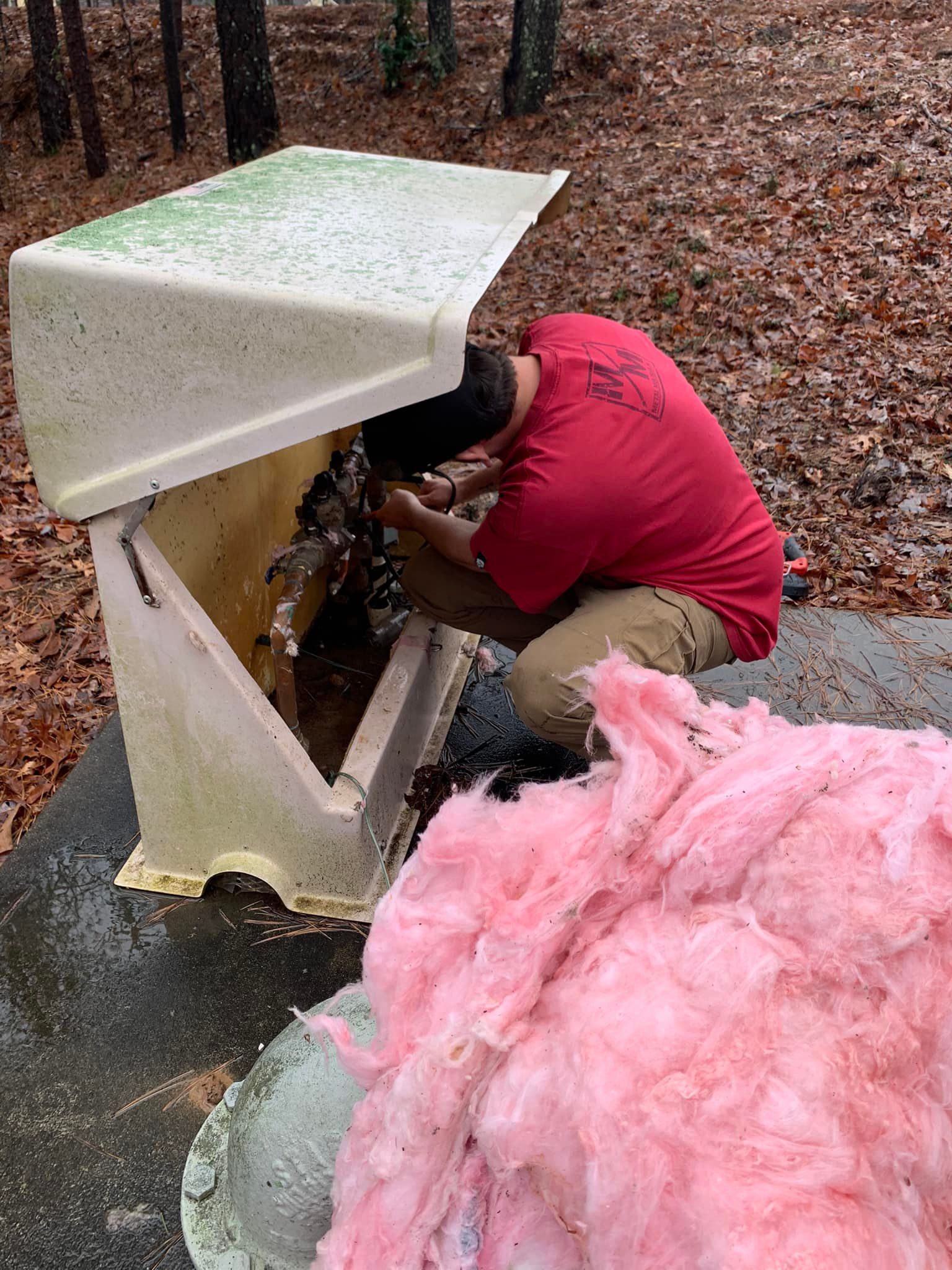 A man in a red shirt is kneeling down next to a pile of pink insulation.