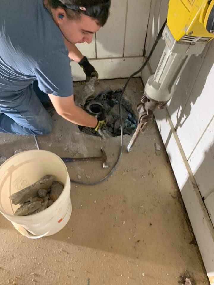 A man is working on a drain in a laundry room.
