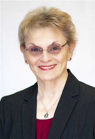 A woman wearing glasses and a black jacket smiles for the camera