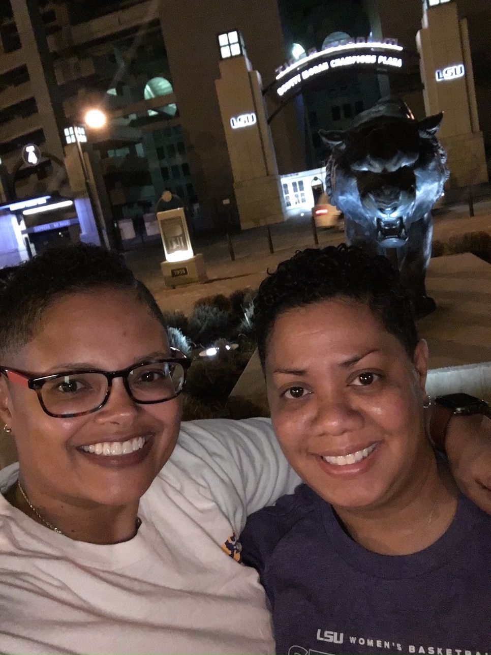 Two women are posing for a picture with a statue in the background