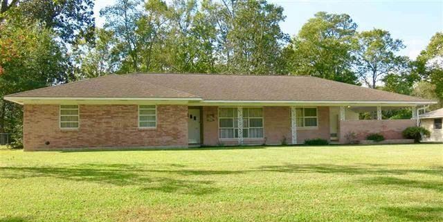 A brick house with a brown roof and a large lawn in front of it.