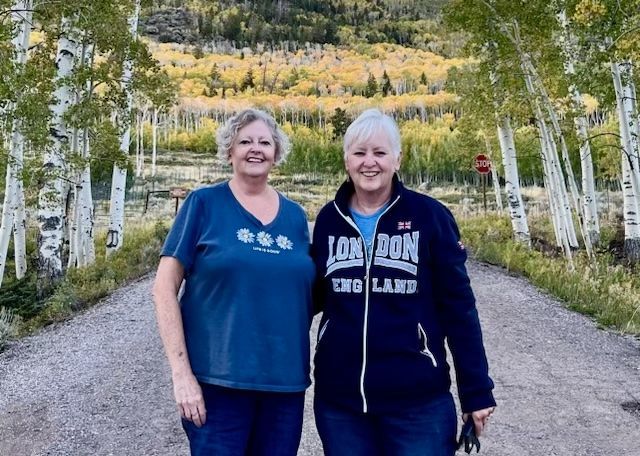 Two women are standing next to each other on a dirt road . one of the women is wearing a london sweatshirt.