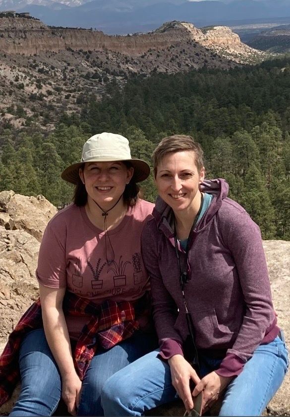 Two women are sitting on a rock in front of a mountain.