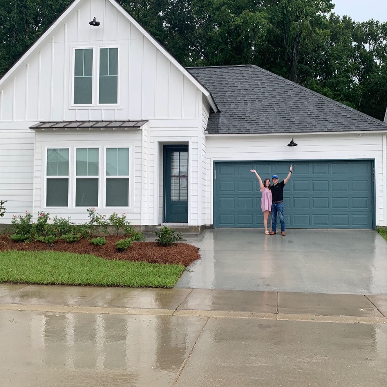 A man and woman are standing in front of a white house with a blue garage door.