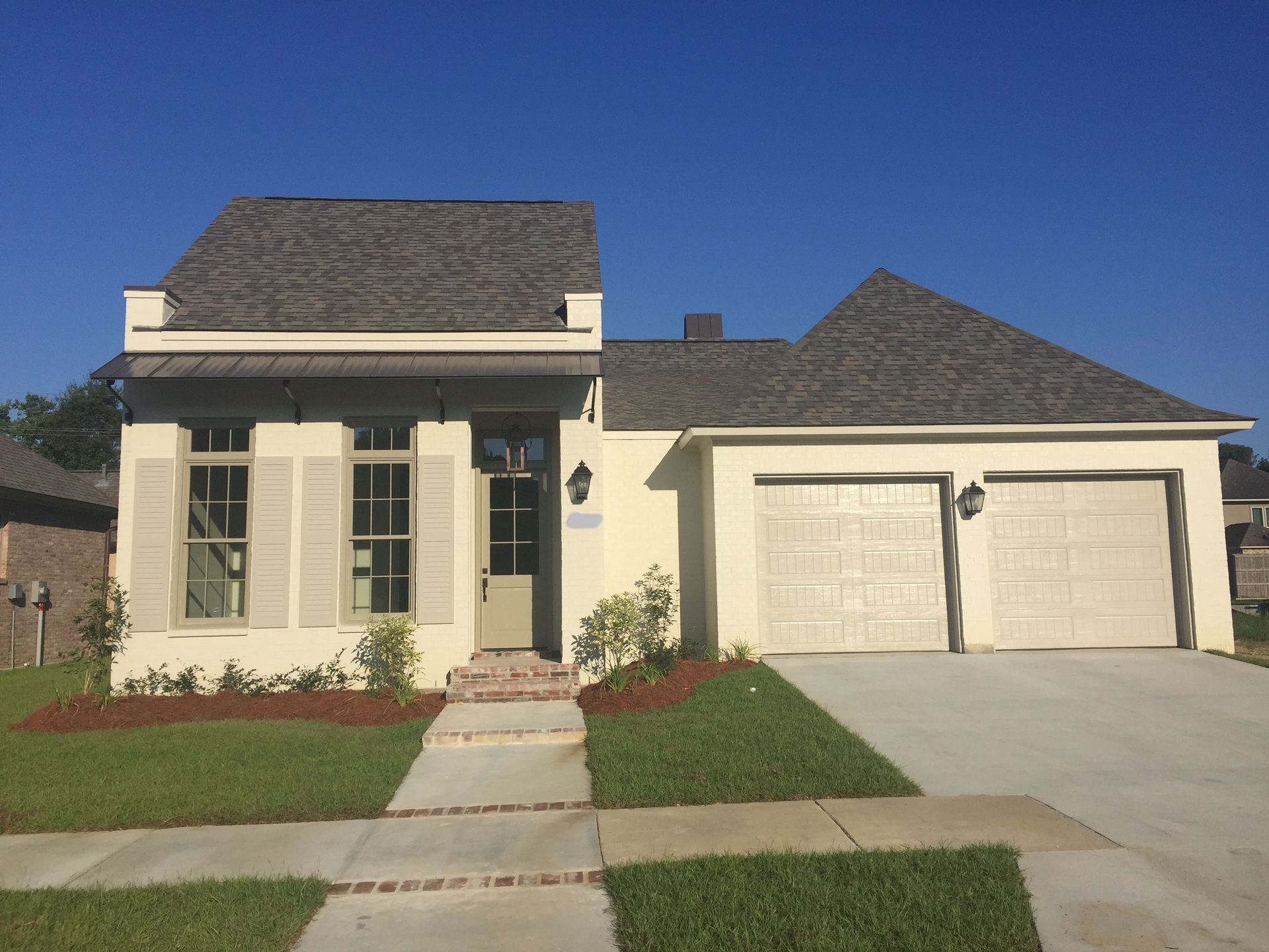 A white house with a gray roof and two garage doors