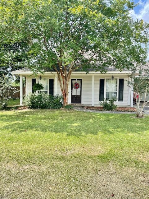 A white house with a porch and a tree in front of it.