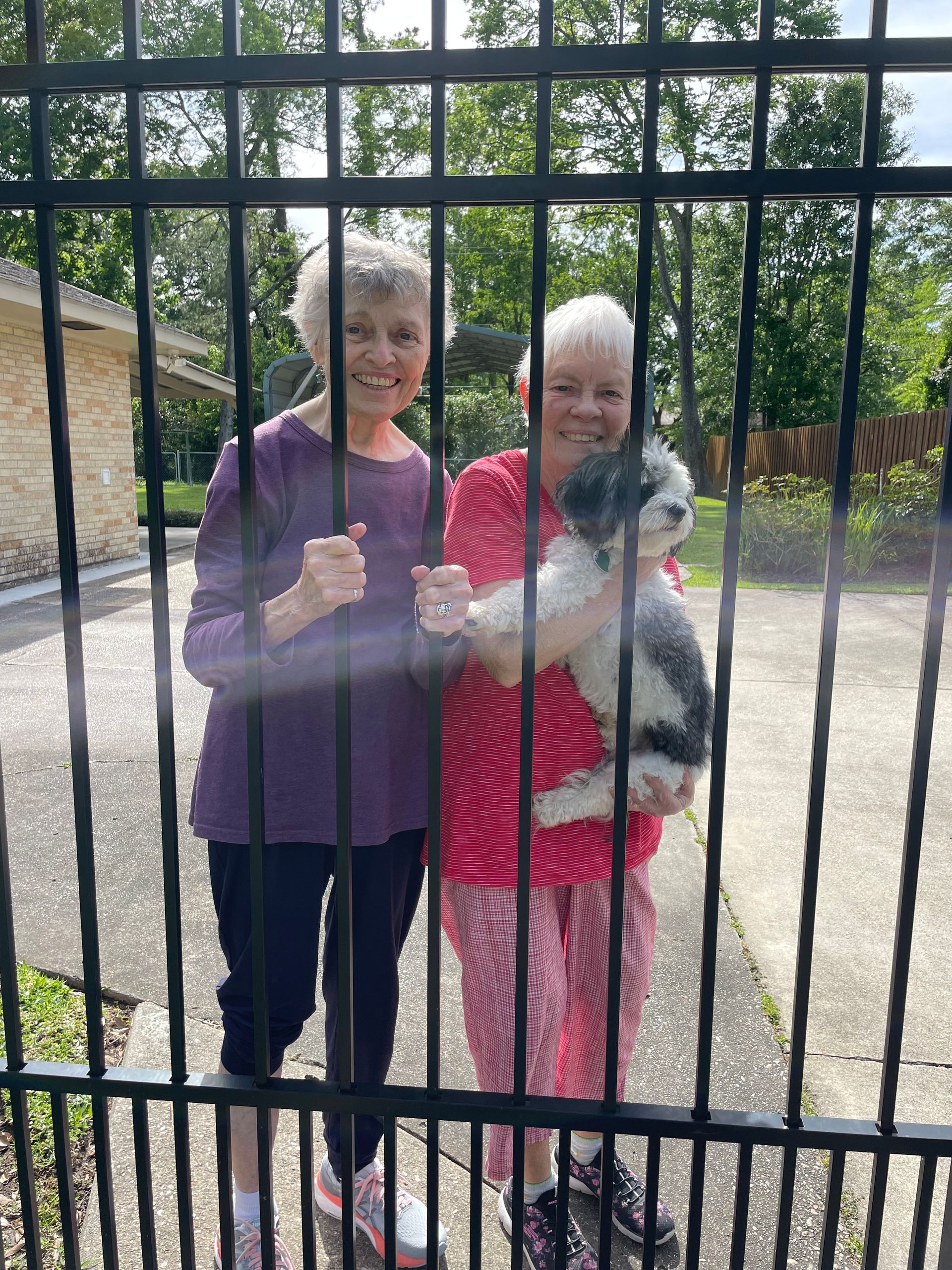 Two women are holding a dog behind a fence.